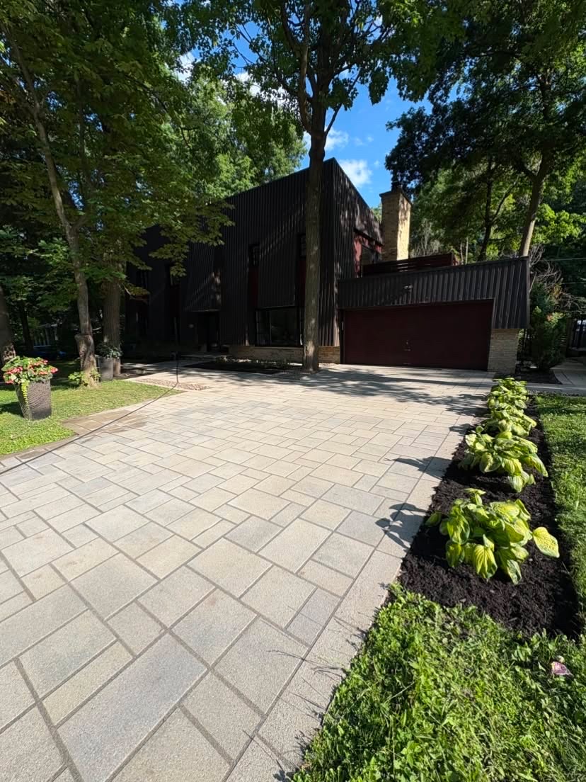 Une entrée en pavés avec une plate-bande de hostas et de paillis devant une maison moderne noire.