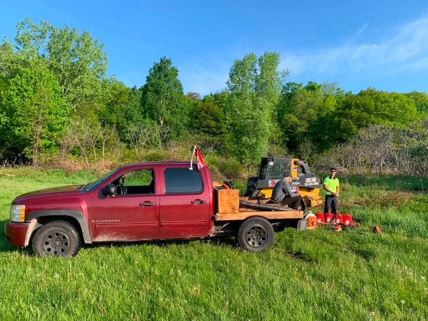 Un camion et une remorque avec un bobcat et de l'équipement de paysagement dans un grand terrain gazonné.