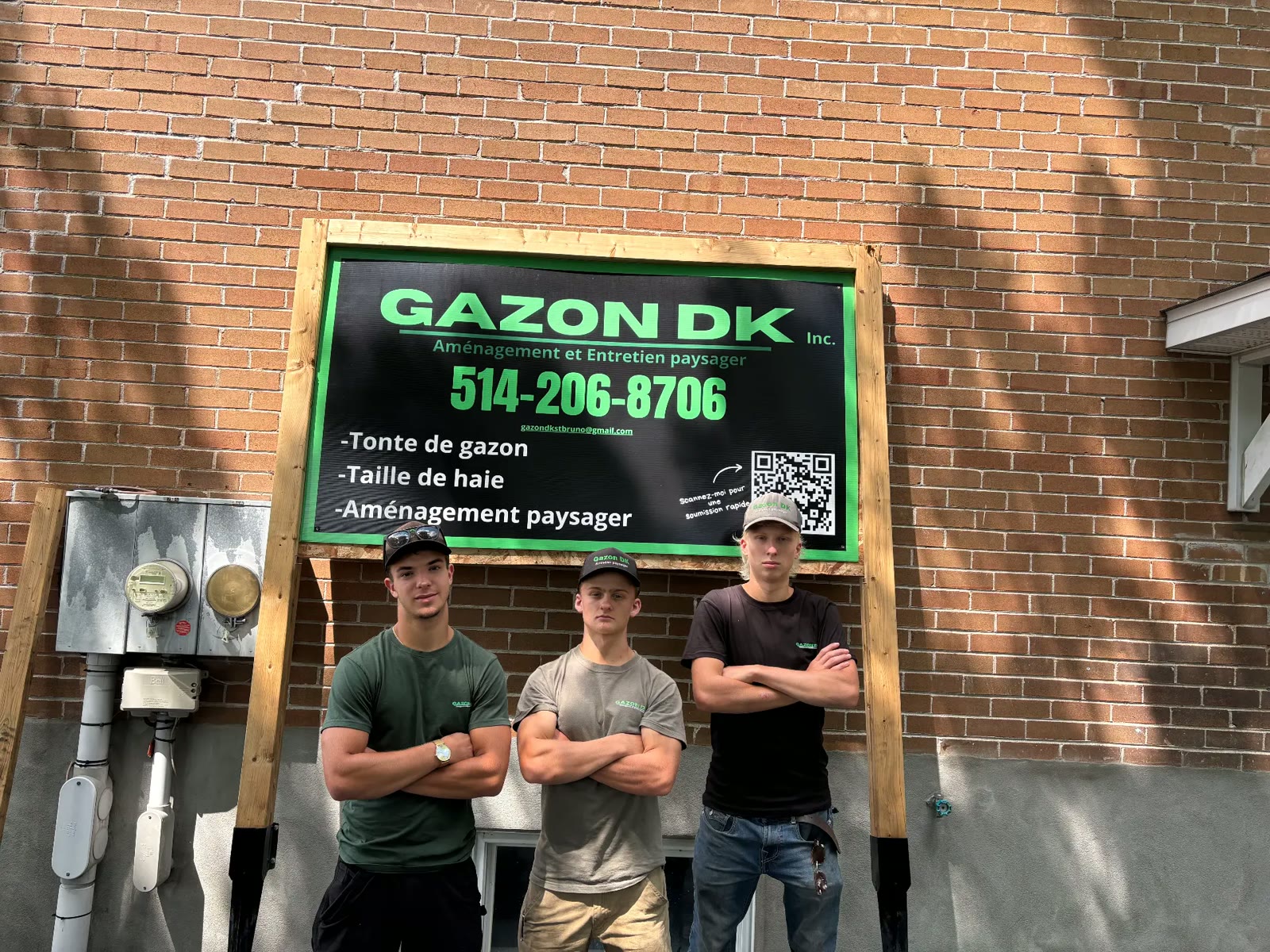Luka, Kimi et Denis, les trois copropriétaires de Gazon DK, bras croisés devant l'affiche de l'entreprise.
