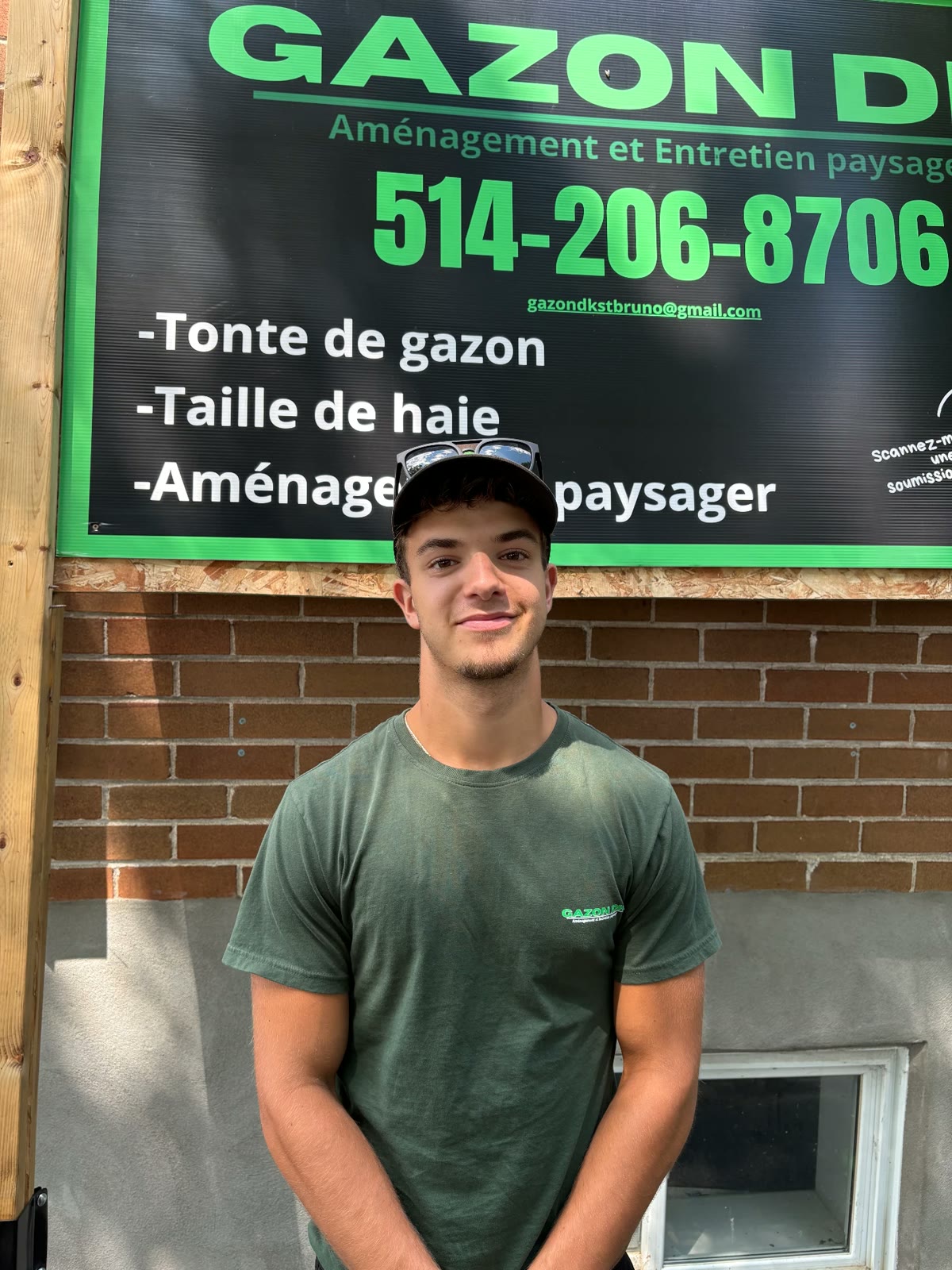 Luka, copropriétaire de Gazon DK, en t-shirt vert devant l'affiche de l'entreprise.